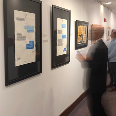 text message art pieces hanging on wall in black frames in a gallery with a motion blurred person looking at them