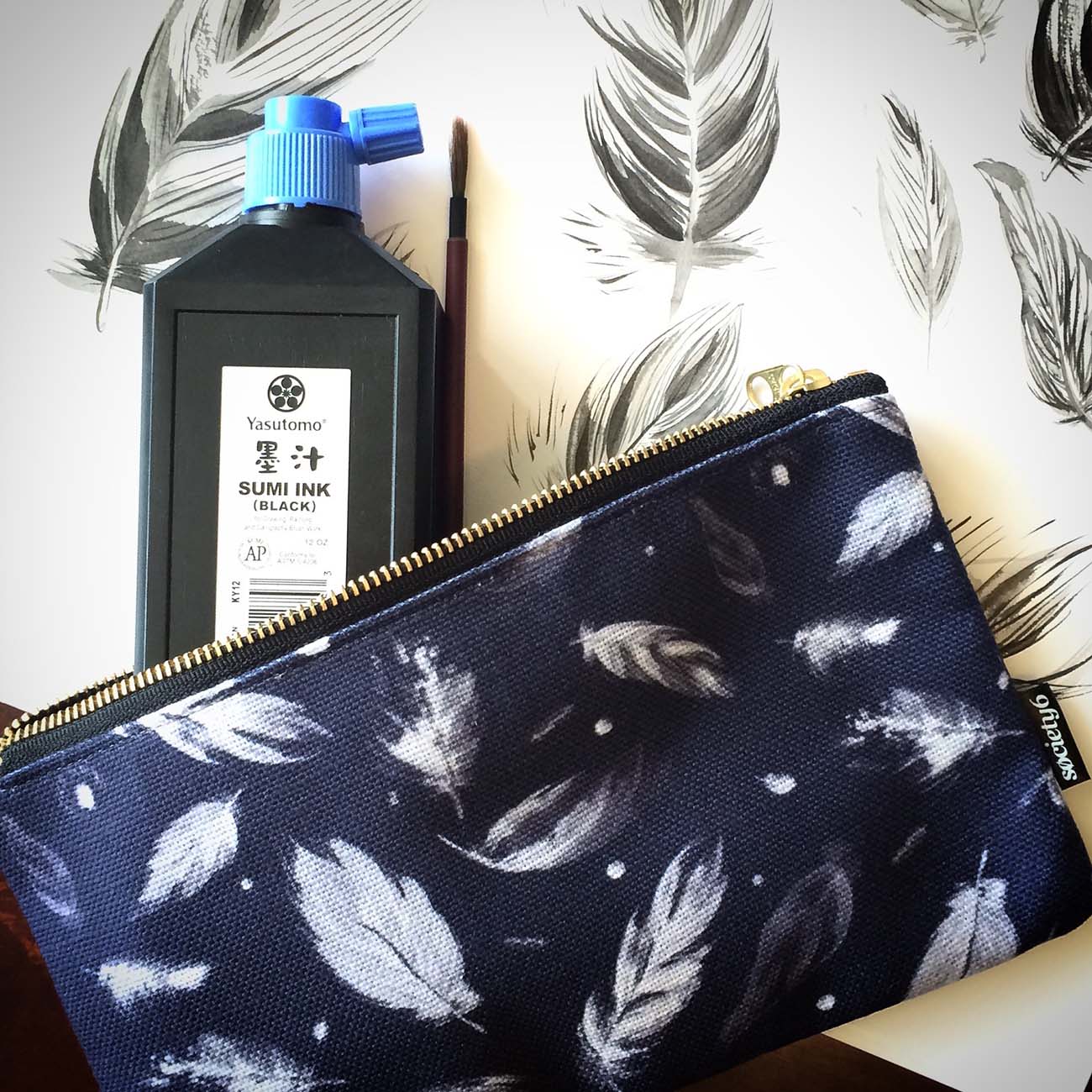 navy and blue feather patterned zip pouch with ink and brush poking out on the sketches that became the pattern