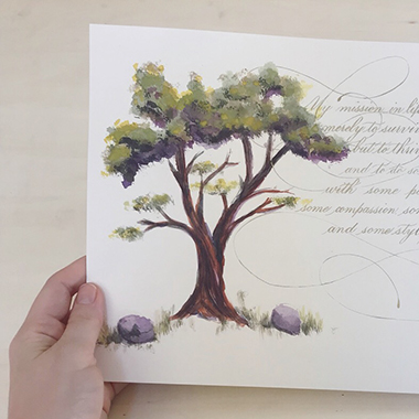 hand holding art piece with painted cypress tree and golden copperplate lettering connected with flourishes